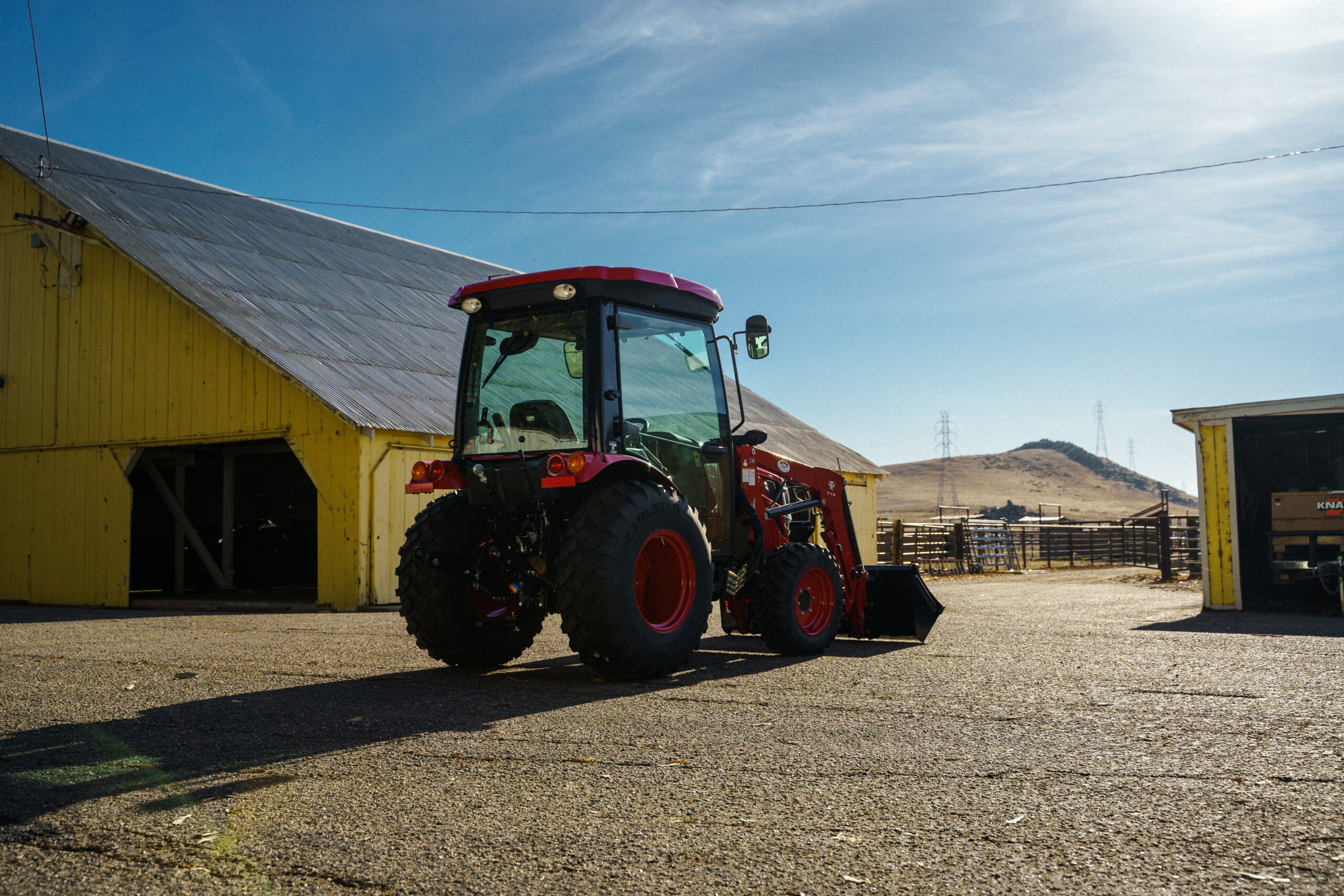 Red tractor with Carlstar Versa Turf tires parked in front of a yellow barn on a dirt road.